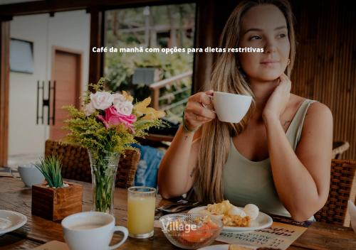 een vrouw aan een tafel met een kopje koffie bij Village Praia do Rosa in Praia do Rosa