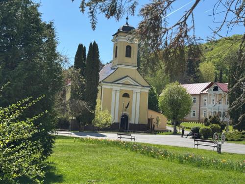 a church with a clock tower in the middle of a park at Penzion Zornicka in Bardejovské Kúpele