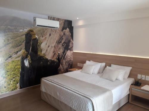 a bedroom with a bed with a painting on the wall at Suíte Vista Azul - Banheira com vista Pedra Azul in Pedra Azul