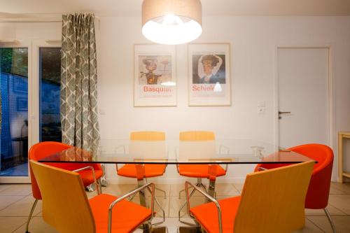 une salle à manger avec une table en verre et des chaises orange dans l'établissement Appartement de standing - 4 chambres - Grand Lyon, à Villeurbanne