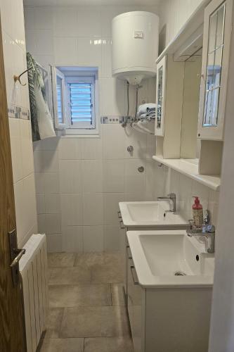 a white bathroom with a sink and a window at Seafront apartment with balcony-50 m from the sea in Šilo