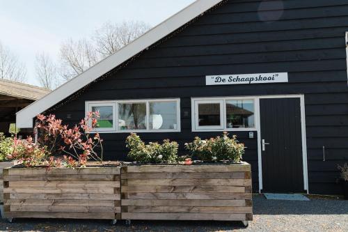 a black house with a door and some flowers at Appartement de Schaapskooi in Heinkensand