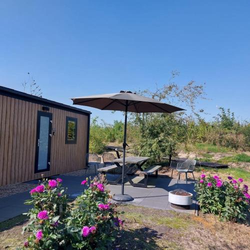 a patio with a table and an umbrella and flowers at De Eend - Tiny house in de Zeeuwse Natuur in Driewegen