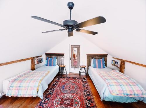 two beds in a room with a ceiling fan at Capt Clarke Historic Homestead Venue in Old Saybrook