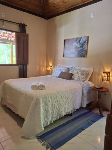 a bedroom with a bed with white sheets and a window at Recanto Verde - Praia de Santo Antônio in Diogo