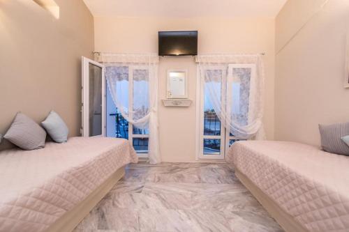 two beds in a room with two windows at Fratelli Family Rooms in Tinos Town