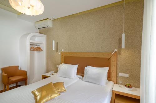 a bedroom with a bed with white sheets and gold pillows at Adriani Hotel in Naxos Chora