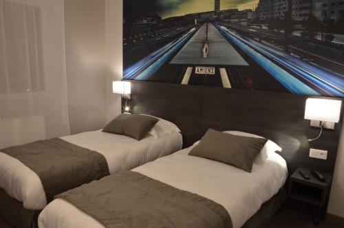 two beds in a hotel room with a picture on the wall at Logis Hôtel - La Chambre d'Amiens in Amiens