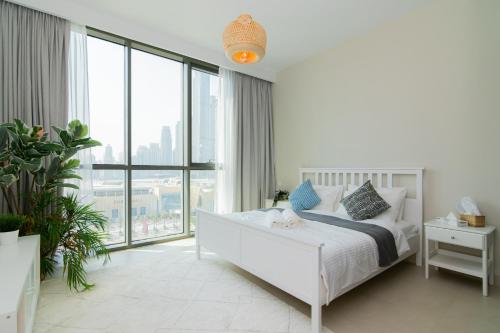 a white bedroom with a bed and a large window at Elite Escape Holiday Home - 2 BHK Getaway with Burj Khalifa View and Dubai Mall Access - 1504 in Dubai