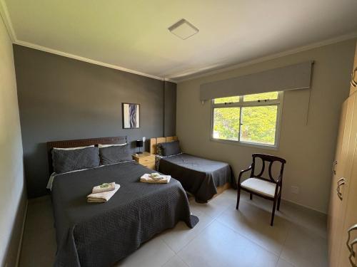 a bedroom with two beds and a chair and a window at Apartamento no centro de São Lourenço e a 750 metros do parque in São Lourenço