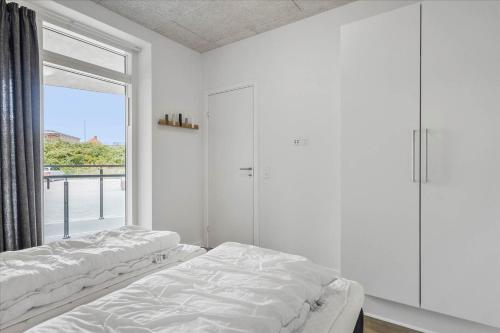 two beds in a white room with a window at Beautiful harbor view apartment in Hvide Sande
