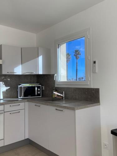 une cuisine avec des placards blancs et une fenêtre avec un palmier dans l'établissement Villa Jasmin vue mer, à Sainte-Marie-la-Mer
