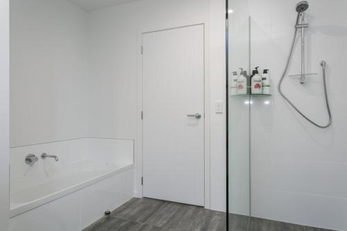 baño blanco con ducha y puerta de cristal en Unwind on Wai, New 4BR Home With Style and Comfort, en Taupo