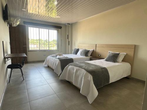 a bedroom with two beds and a desk and a window at Hotel Diamante Sarare 2 in Saravena