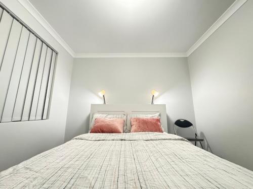 a white bedroom with a bed with two pink pillows at Blissful Modern Home in Perth
