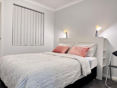 a white bedroom with a bed with two pink pillows at Blissful Modern Home in Perth