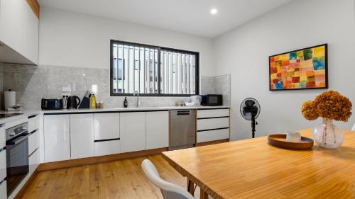a kitchen with white cabinets and a wooden table at Modern Orewa Delight w Parking just Steps to Beach in Orewa