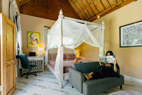 a bedroom with a canopy bed and a woman reading a magazine at The Onion Collective in Ubud