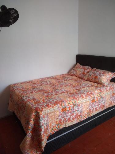 a bed with a flowered blanket and two pillows on it at Quarto e Cozinha em Mongaguá in Mongaguá
