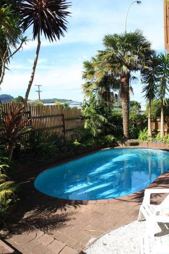 a blue swimming pool in a yard with palm trees at Hosts on the Coast The Harbourview Tairua in Tairua