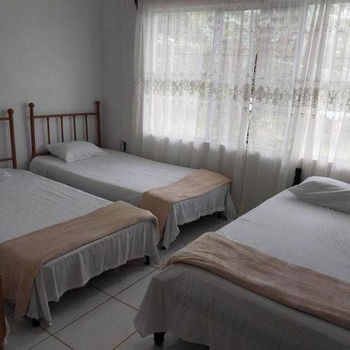 a bedroom with two beds and a window with curtains at Cabaña Gerya in Chachagua