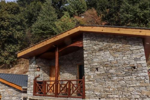 a man standing on a balcony of a stone building at Basho Mud Huts in Vashisht