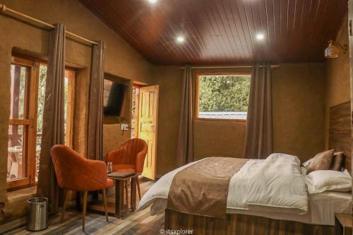 a bedroom with a bed and a chair and a television at Basho Mud Huts in Vashisht