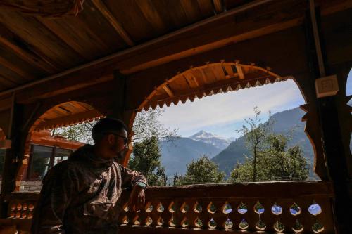 a man standing in front of a window looking at a mountain at Basho Mud Huts in Vashisht