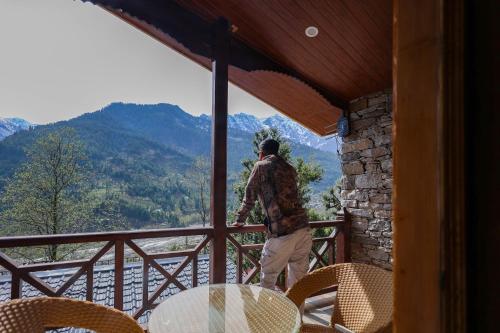 a man standing on a balcony looking out at the mountains at Basho Mud Huts in Vashisht