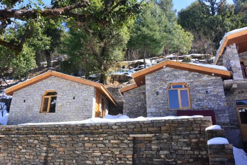 a stone house with a stone wall in the snow at Basho Mud Huts in Vashisht