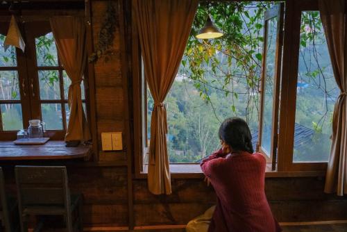 a woman sitting in front of a window looking out at Cú Trên Cây Homestay in Xuan An