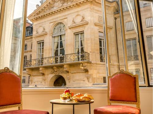 une chambre avec deux chaises et une table en face d'un bâtiment dans l'établissement Merveil Signature Suite - Valois - Louvre view, à Paris