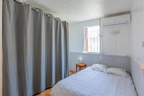 - une chambre avec un lit et un rideau gris dans l'établissement Le Robinson - proche plage, à Marseillan