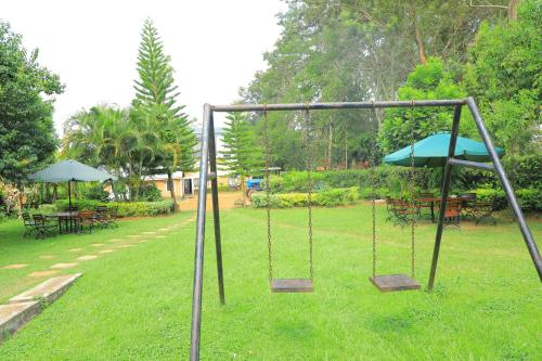 a swing set in a park with tables and umbrellas at Pereto Gardens in Gatunga