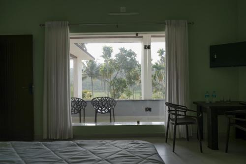 a bedroom with a window with two chairs and a table at The Calm County Homestay in Mānantoddy