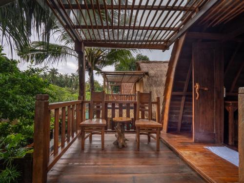 a wooden porch with two chairs and a cat sitting on it at Aruna Jayanti Villa in Tejakula
