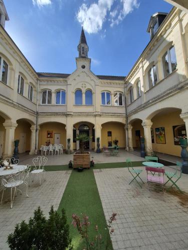 un grand bâtiment avec une cour dotée de tables et de chaises dans l'établissement Motel le Bon Samaritain, à Roucy