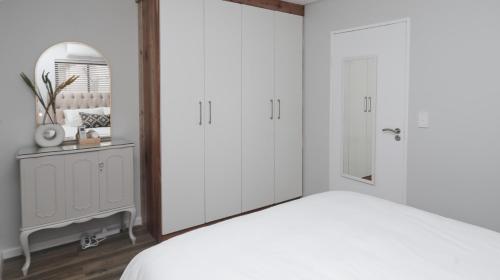 a bedroom with white cabinets and a bed with a mirror at Happy Days in Paarl