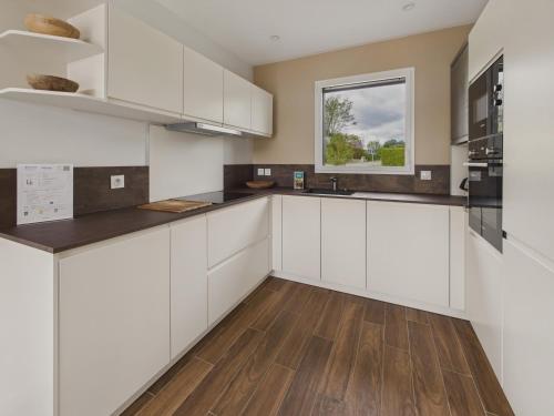 une cuisine avec des armoires blanches et un plancher en bois dans l'établissement Maison neuve avec terrasse et jardin pour 6, à Fouesnant
