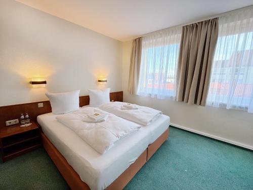 a large bed in a hotel room with a large window at REGIOHOTEL Bunte Stadt in Wernigerode