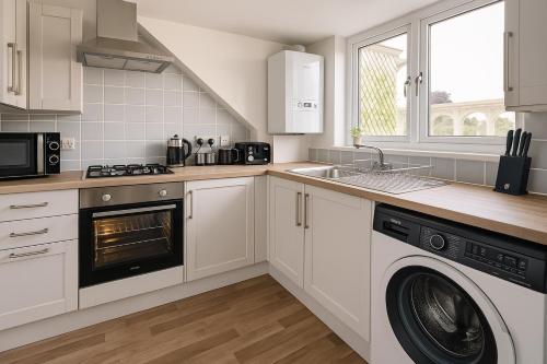 a kitchen with white cabinets and a washer and dryer at Nestee Serviced Apartments - Central Torquay - Pet Friendly - Harbour Views in Torquay