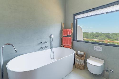 a bathroom with a tub and a toilet and a window at Monte da Torre in Melides