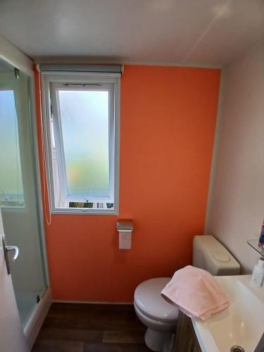 La salle de bains orange est pourvue de toilettes et d'une fenêtre. dans l'établissement Mobil-Home le Montourey, à Fréjus