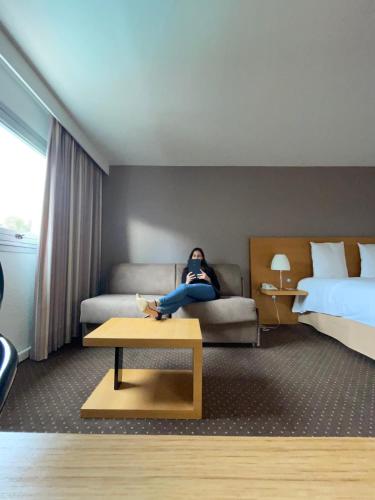 a woman sitting on a couch in a hotel room at Mercure Bordeaux Lac in Bordeaux