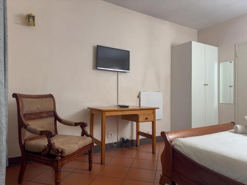 a bedroom with a chair and a desk with a television at Park Gables Loftus Guest House in Pretoria