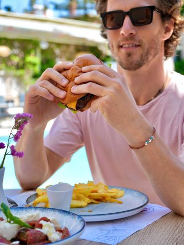 a man sitting at a table eating a hamburger at Telesilla Hotel in Kontokali