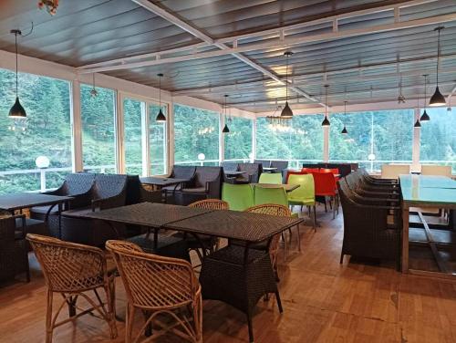 a dining room with tables and chairs and windows at Hotel Narayana Palace in Harsil