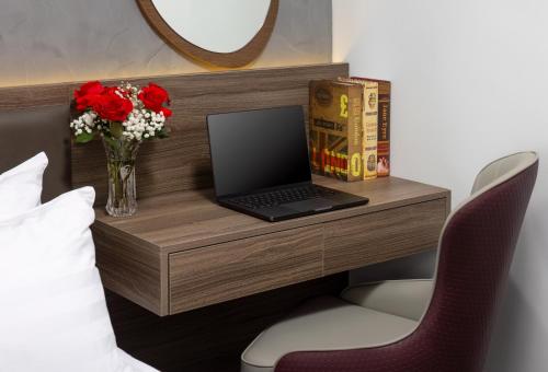 a desk with a laptop on it with a vase of flowers at Cat Ba Wistaria Hotel- Jacuzzi Rooftop & Fitness in Cat Ba