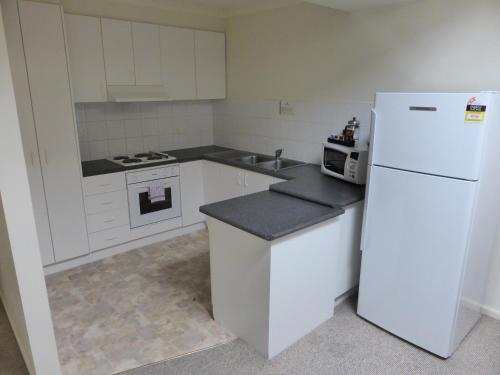 a white kitchen with a refrigerator and a microwave at Lifestyle Apartments at Ferntree in Fern Tree Gully