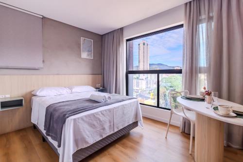 a bedroom with a bed and a desk and a large window at Loft Novo todo Mobiliado com WIFI Piscina e próximo a Oktober in Blumenau